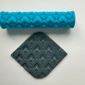 May include: A blue rolling pin with a geometric pattern and a dark grey piece of clay with the same pattern.