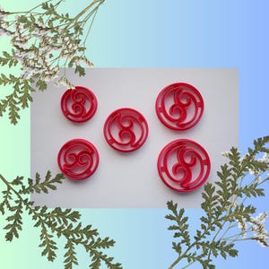 Puede incluir: Cinco cortadores de galletas de plástico rojo en forma de un número ocho estilizado. Los cortadores están sobre una superficie blanca.