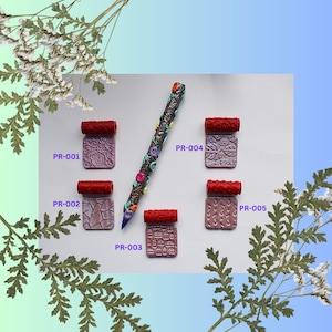 Peut inclure: Cinq tampons à roulettes en argile polymère différents avec des poignées rouges et un rouleau à pâtisserie à motifs colorés. Les tampons sont étiquetés PR-001, PR-002, PR-003, PR-004 et PR-005.