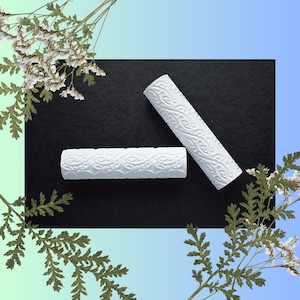 May include: Two white textured rollers with a decorative pattern on a black surface.