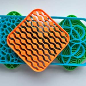 May include: Three colorful silicone dish drying mats with different geometric patterns. The top mat is orange with a wavy pattern, the middle mat is blue with a web-like pattern, and the bottom mat is green with a floral pattern.