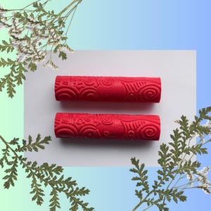 Peut inclure: Deux rouleaux à pâtisserie rouges avec un motif en spirale sur la surface. Les rouleaux à pâtisserie sont sur un fond blanc.