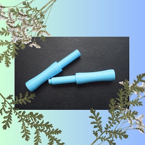 May include: Two light blue plastic applicators, one is extended and the other is closed, on a black surface.