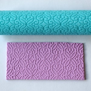 May include: Two rolling pins for baking, one is turquoise blue and the other is lavender purple. Both have a decorative embossed pattern.