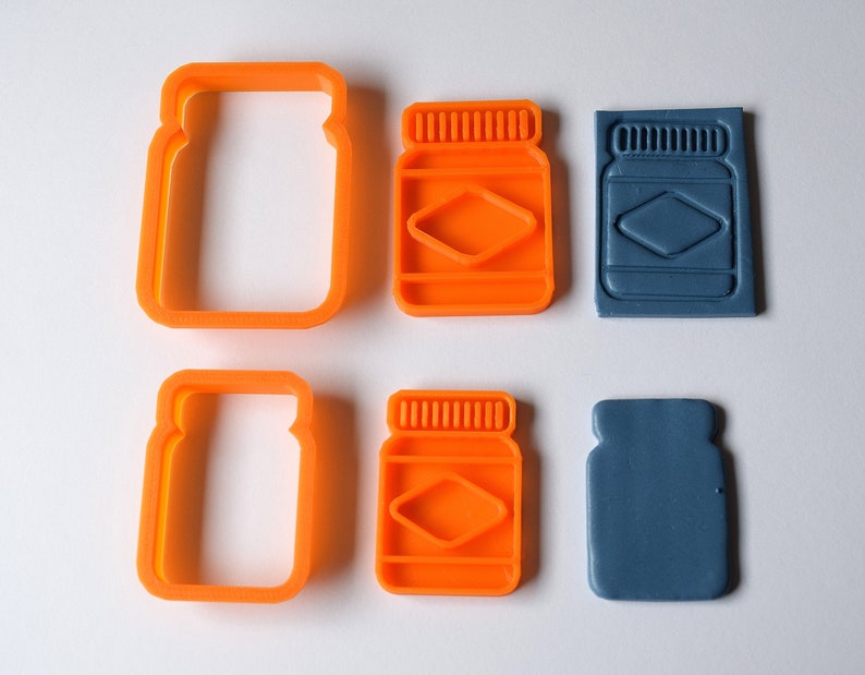 May include: Two orange plastic cookie cutters shaped like jars with lids, and two blue plastic cookie cutters shaped like jars with lids.