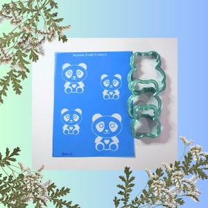 Puede incluir: Una lámina de plástico azul con el texto "Aussie Craft Cutters" y cuatro contornos de osos panda blancos. Tres cortadores de galletas de oso panda azul turquesa están apilados encima de la lámina.