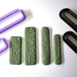May include: Four green polymer clay strips with a floral pattern, two purple plastic rectangle-shaped cookie cutters, and two black plastic rectangle-shaped cookie cutters.
