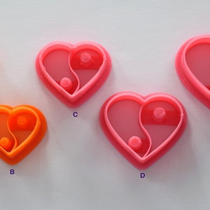 Puede incluir: Cinco cortadores de galletas en forma de corazón, dos naranjas y tres rosas, con un diseño de yin-yang. Los cortadores están etiquetados con A, B, C, D y E.