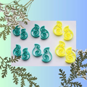 May include: Six plastic cookie cutters in the shape of a stylised swirl. Two are teal, two are yellow, and two are a lighter shade of teal.