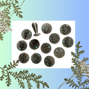 Peut inclure: Un ensemble de 12 tampons métalliques ronds avec différents motifs de feuilles. Les tampons sont disposés en cercle autour d'une poignée en métal. Les tampons sont utilisés pour créer des empreintes dans l'argile, la cire ou d'autres matériaux mous.
