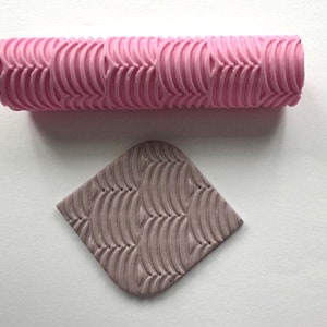 May include: A pink rolling pin with a wavy pattern and a matching pink clay imprint with the same pattern.