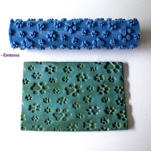 May include: A blue rolling pin with a paw print design. The rolling pin is used to create an embossed paw print pattern on a green surface.