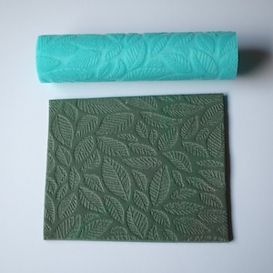 May include: Two silicone rolling pins with a leaf pattern. The top rolling pin is turquoise blue and the bottom rolling pin is dark green.