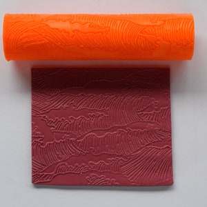 Puede incluir: Un rodillo naranja con un diseño de patrón de onda. El rodillo se utiliza para crear una impresión en una superficie roja.
