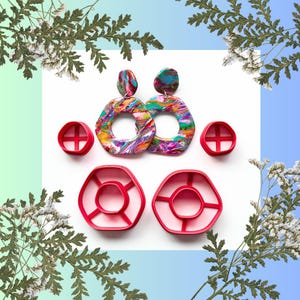 Può includere: Un paio di orecchini astratti e colorati con taglierini in argilla polimerica rossi abbinati. Gli orecchini hanno un effetto marmorizzato con sfumature di rosa, giallo, blu e verde. I taglierini hanno la forma degli orecchini.