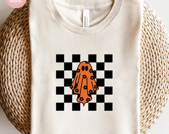May include: A white t-shirt with a checkered pattern and an orange ghost with floral details in the center. The text "SVG - PNG - DXF INSTANT DOWNLOAD" is at the bottom of the image.