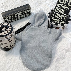 K&ouml;nnte beinhalten: Ein grauer Kapuzenpullover f&uuml;r einen Hund, mit dem Text "There is always room for one more dog" auf einem Holzschild im Hintergrund.  Das Schild "Life without dogs... I don't think so" ist ebenfalls im Hintergrund zu sehen.