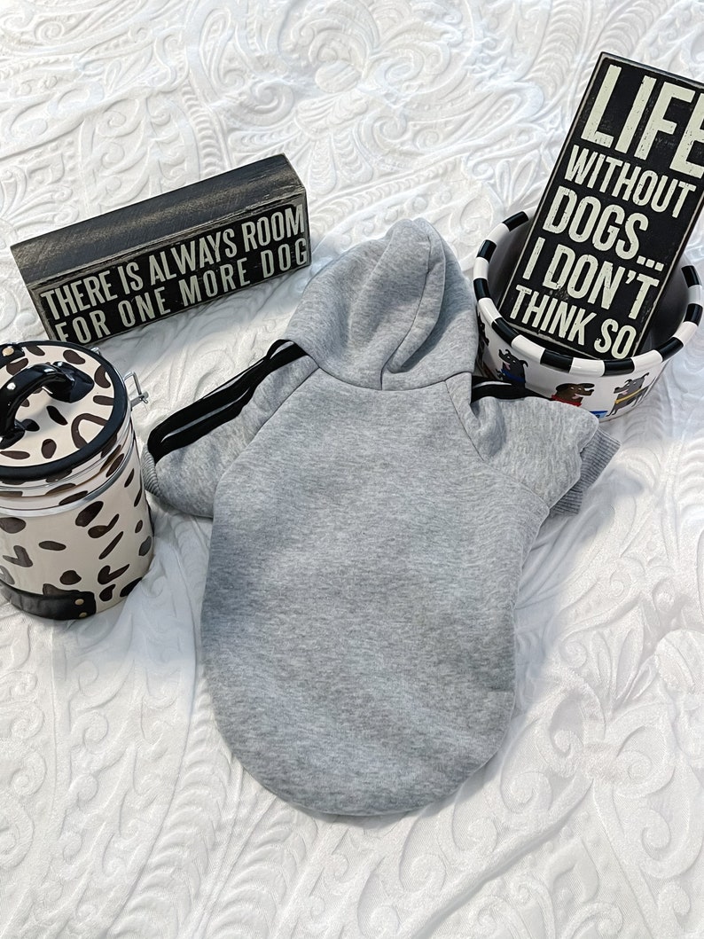 K&ouml;nnte beinhalten: Ein grauer Kapuzenpullover f&uuml;r einen Hund, mit dem Text "There is always room for one more dog" auf einem Holzschild im Hintergrund.  Das Schild "Life without dogs... I don't think so" ist ebenfalls im Hintergrund zu sehen.