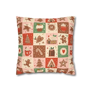 Puede incluir: Cojín cuadrado con un diseño de patchwork con galletas de jengibre, casas de jengibre, árboles de Navidad y copos de nieve en tonos de rojo, verde, rosa y marrón. El cojín tiene un fondo blanco.