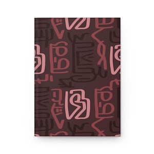 May include: A closed hardcover journal with a dark brown cover. The cover displays a repeating pattern of abstract shapes in pink and brown hues. The journal has a clean, minimalist design.