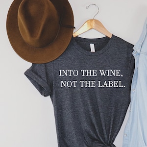 May include: A dark heather grey t-shirt with the text "INTO THE WINE, NOT THE LABEL." printed in white.