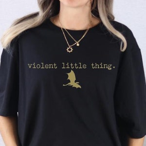 May include: Black oversized t-shirt with the text "violent little thing." and a gold silhouette of a bat.