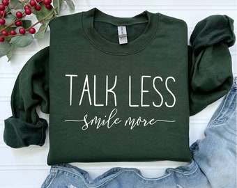 May include: A dark green sweatshirt with the text "TALK LESS smile more" in white.