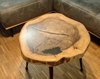 May include: A round wooden coffee table with a natural wood finish and black epoxy resin inlay. The table has a live edge design and sits on four black metal legs.
