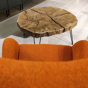May include: A close-up view of an orange armchair with a wooden coffee table with black hairpin legs in the background.