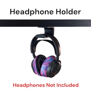 May include: A black headphone holder attached to the underside of a desk. The holder is designed to hold headphones with a headband. The headphones are not included. The text "Headphone Holder" is at the top of the image and the text "Headphones Not Included" is at the bottom of the image.