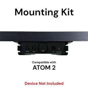 May include: Black mounting kit for a music device. The kit includes a bracket that attaches to a shelf or desk and a plate that holds the device. The text "Mounting Kit" is at the top of the image. The text "Compatible with ATOM 2" is in the middle of the image. The text "Device Not Included" is at the bottom of the image.
