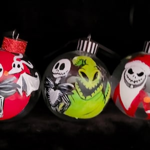 May include: Three hand-painted glass Christmas ornaments featuring characters from The Nightmare Before Christmas. The first ornament features Jack Skellington and Zero, the second ornament features Jack Skellington and the Grinch, and the third ornament features Jack Skellington dressed as Santa Claus and Zero.