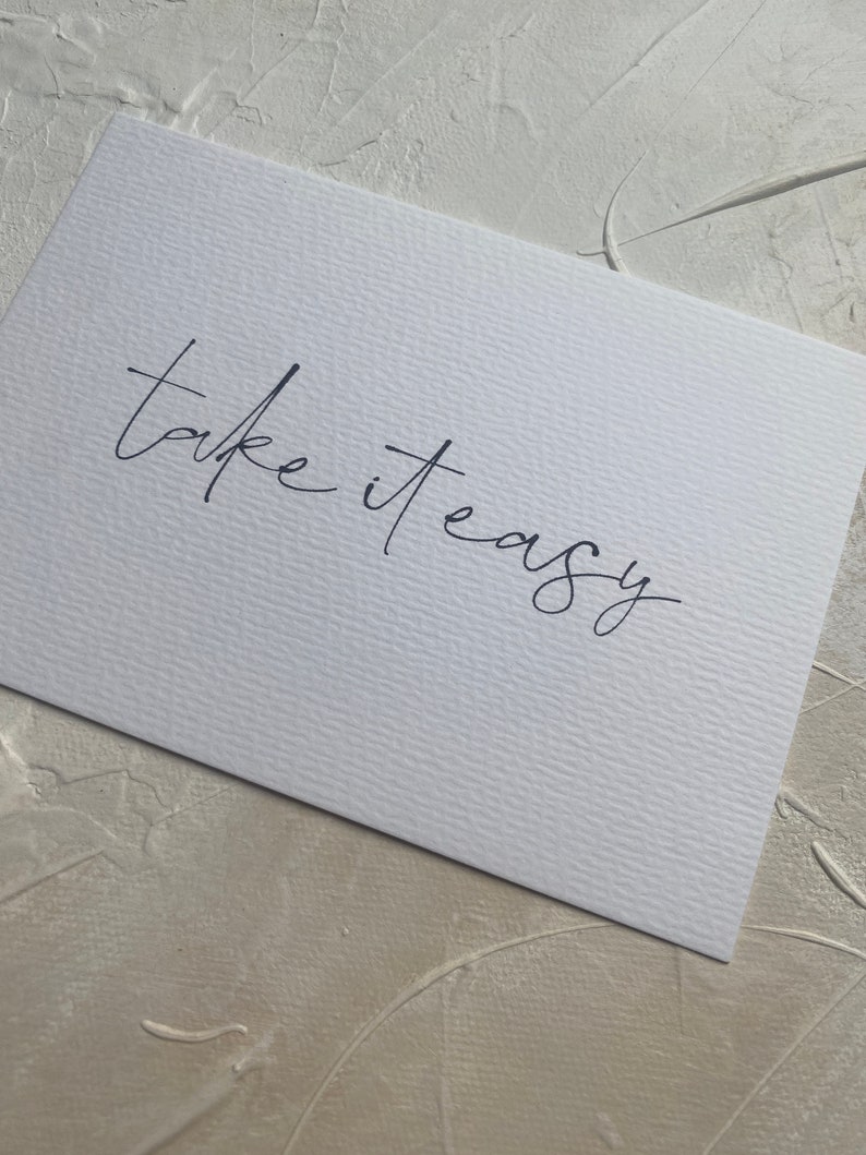 Puede incluir: Tarjeta blanca con la frase manuscrita "take it easy" en tinta negra.
