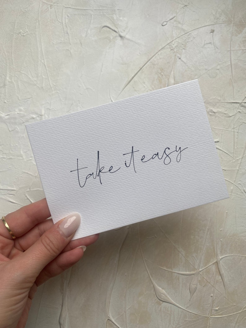 Puede incluir: Tarjeta blanca con el texto "take it easy" escrito en cursiva negra.