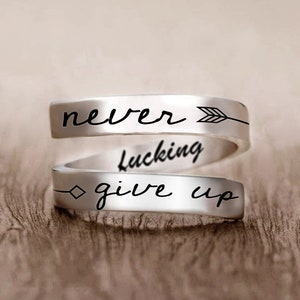 May include: Silver ring with the words "never giving up" and an arrow engraved on it.