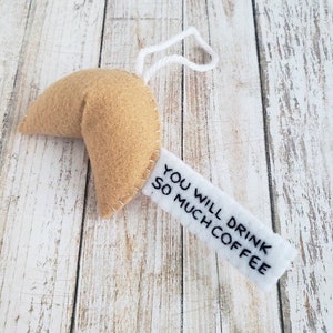 May include: A felt fortune cookie ornament with a white tag that reads "You will drink so much coffee".
