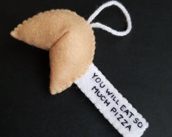 May include: A felt fortune cookie ornament with a white tag that reads "You will eat so much pizza".
