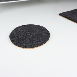 A single circle felt and cork coaster in black felt shown on a white desk surface next to matching black wool felt desk mat.