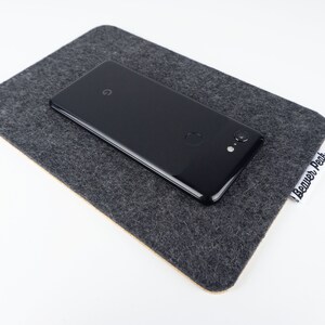 A large black phone mat shown on a white desk with a black phone on top.