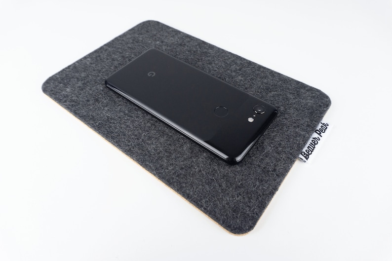 A large black phone mat shown on a white desk with a black phone on top.