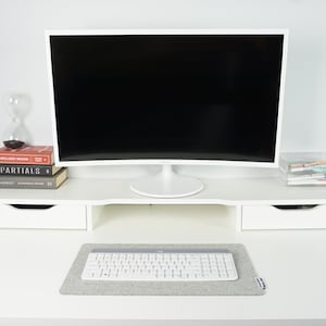 Smallest size (18 x 11 inch) desk mat in light grey color. Desk mat is mostly filled up by white keyboard with white mouse sitting off of the desk mat.