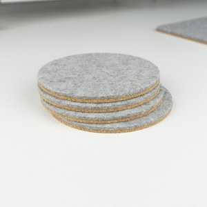 May include: A set of four gray felt coasters with cork backing. The coasters are stacked on top of each other.