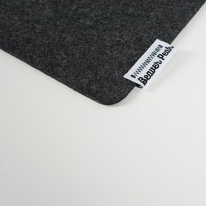 Close up of black desk mat corner with Beaver Peak logo on one edge. The logo is made of white cotton with a black embroidered Beaver Peak logo and black stitching to attach it to the desk mat. The logo protrudes from the desk mat edge.