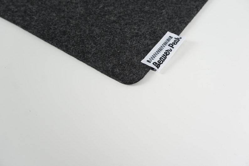 Close up of black desk mat corner with Beaver Peak logo on one edge. The logo is made of white cotton with a black embroidered Beaver Peak logo and black stitching to attach it to the desk mat. The logo protrudes from the desk mat edge.