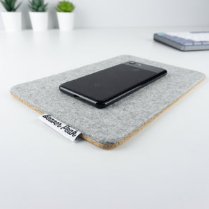 Grey wool felt and cork phone mat with an iPhone on top, shown on a white desk surface.