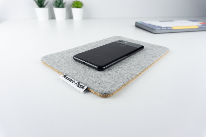 Grey wool felt and cork phone mat with an iPhone on top, shown on a white desk surface.