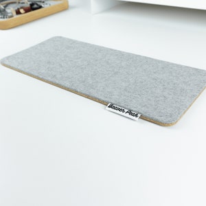 Empty grey merino wool felt and cork keyboard mat on white desk.