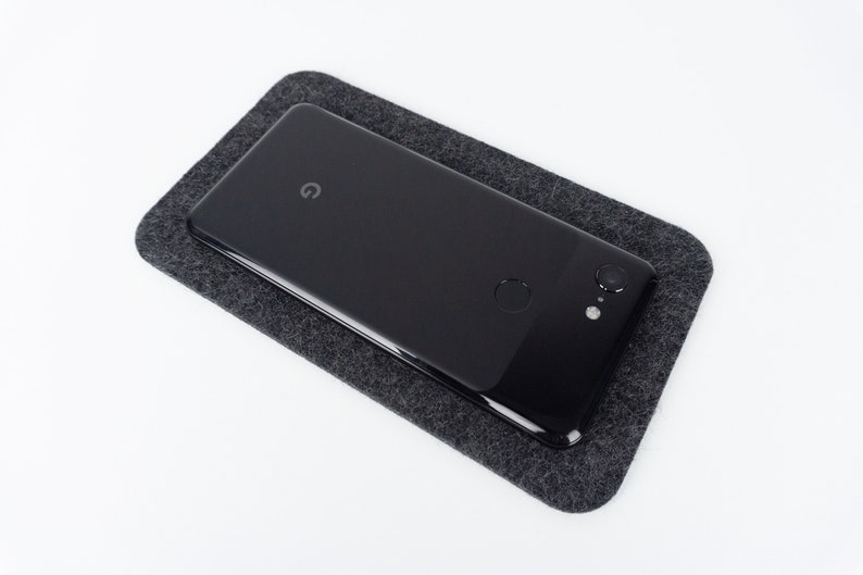 A small black phone mat shown on a white desk with an iPhone on top.