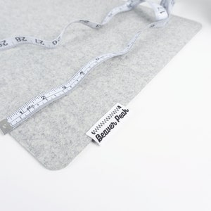May include: A gray felt fabric with a white measuring tape and a white label with the text "Beaver Peak" printed on it.