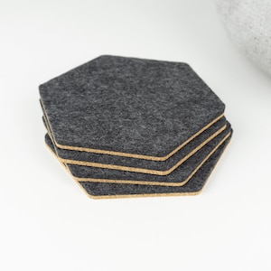Puede incluir: Un juego de cuatro posavasos de fieltro gris con respaldo de corcho. Los posavasos son hexagonales y tienen una textura sutil.